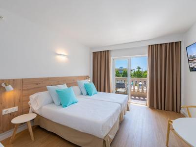 Camera d'albergo luminosa con letto matrimoniale, pavimento in legno e balcone con vista giardino.