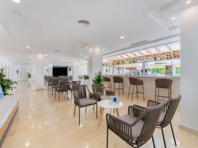 Area lounge moderna dell'hotel con sedie, tavoli e bar in uno spazio luminoso con tetto in vetro.