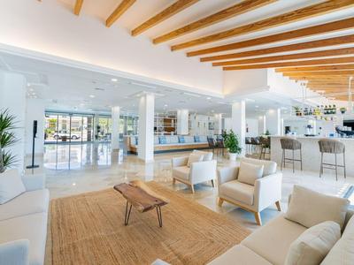 Lounge dell'hotel luminosa con mobili bianchi, travi di legno e area bar