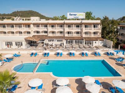 Grande hotel con piscina e ombrelloni davanti a una collina sotto un cielo sereno.