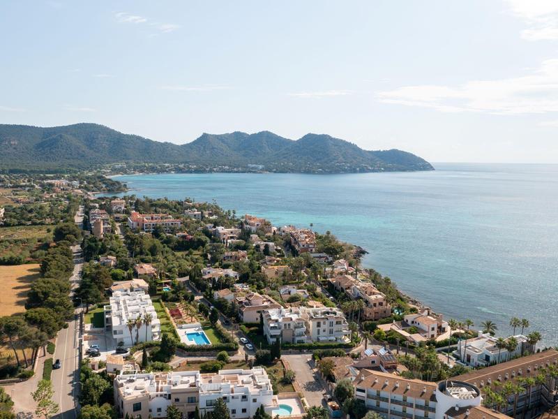 Vista di una città costiera con hotel, piscina, montagne e mare calmo all'orizzonte.