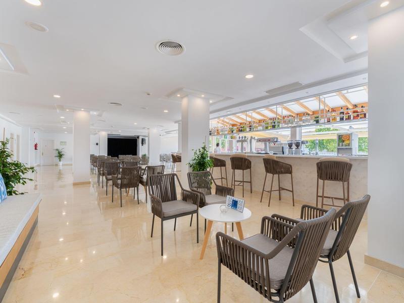 Area lounge moderna dell'hotel con sedie, tavoli e bar in uno spazio luminoso con tetto in vetro.