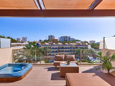 Moderne Terrasse mit Jacuzzi, Couch und Blick auf Gebäude und Palmen unter blauem Himmel.