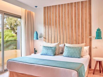 Camera d'hotel moderna con letto matrimoniale, accenti turchesi e balcone con piante.