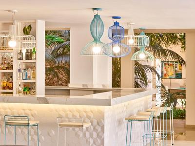 Moderner Hotelbarbereich mit weißen Möbeln und farbigen Hängelampen.