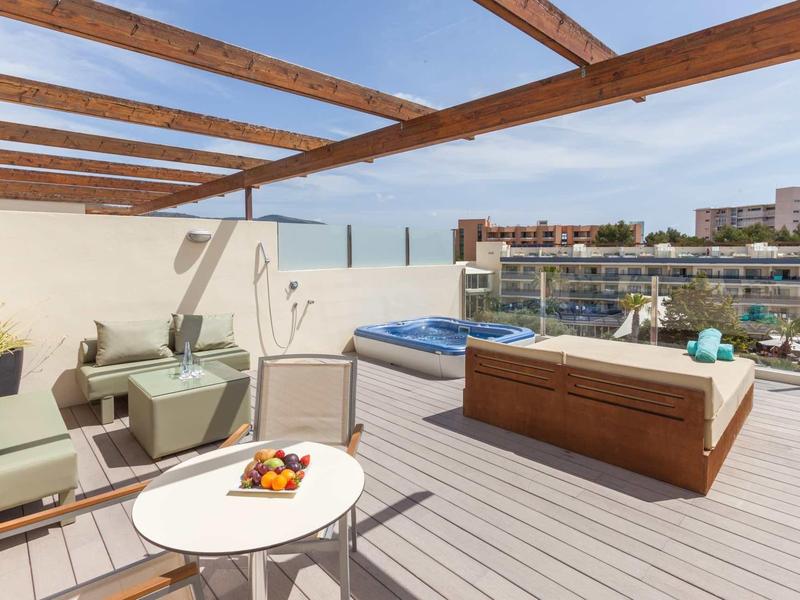 Amplia terraza en la azotea con zona de estar, jacuzzi y vista a la ciudad bajo cielo despejado.