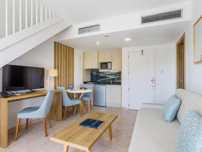 Apartamento acogedor con cocina, mesa de comedor, sofá y televisor bajo una escalera.