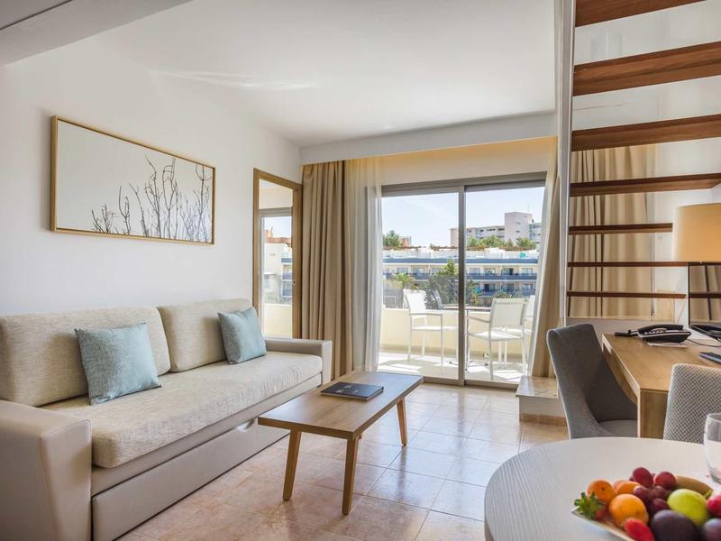 Sala acogedora con sofá, mesa de centro y ventana grande con acceso al balcón.