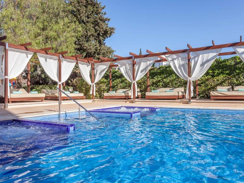 Piscina con agua clara y cortinas blancas, rodeada de árboles y terraza solar.