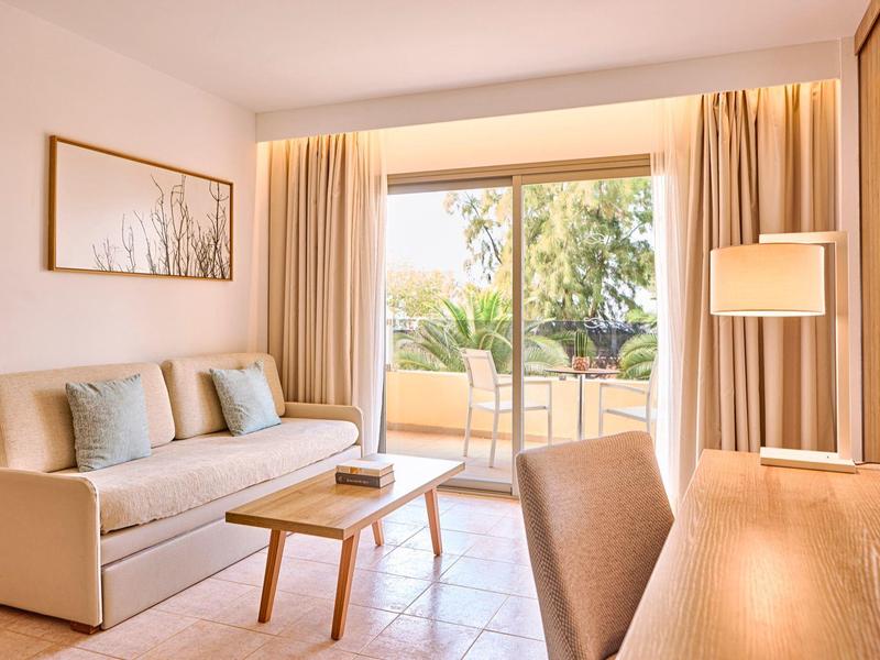 Helles Wohnzimmer mit Sofa, Tisch und Schreibtisch vor einer großen Balkontür