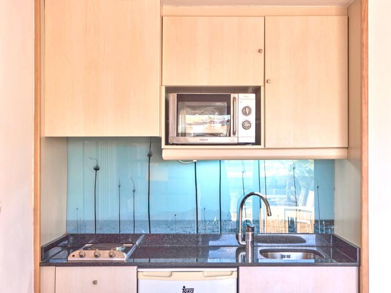 Kleine moderne Küchenecke mit Herd, Spüle und Mikrowelle in Holzschränken.