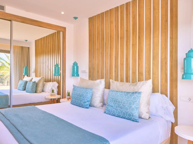 Modernes Hotelzimmer mit gemütlichem Bett, blauen Akzenten und spiegelnder Wand mit Blick auf Terrasse.