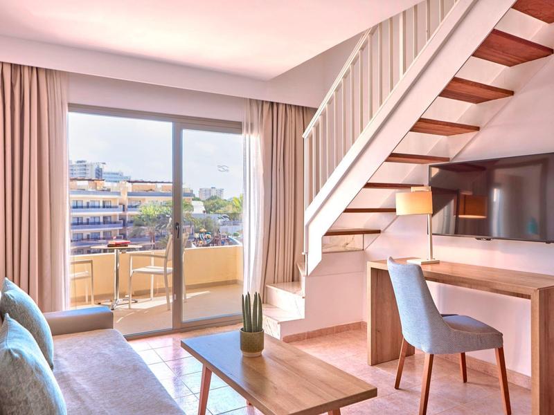 Modernes Hotelzimmer mit Treppe, Schreibtisch, TV und Balkon mit Stadtblick.