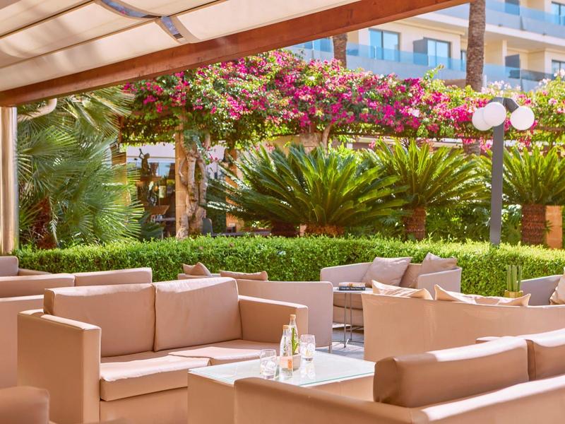 Gemütliche Sitzplätze auf der Terrasse eines Hotels mit grüner Bepflanzung und Blumen.