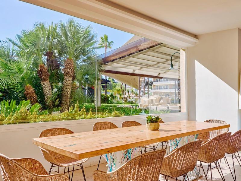 Terrasse mit Holz-Esstisch und Stühlen, Blick auf tropische Gartenlandschaft mit Palmen.
