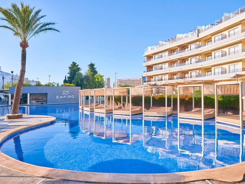 Moderner Pool mit Barstühlen im Wasser und Liegebereichen in einem Hotelresort bei Sonnenschein.