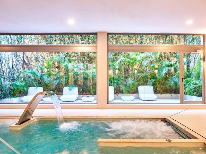 Innen-Pool mit Wasserspiel und großen Fenstern mit Blick auf einen Garten.