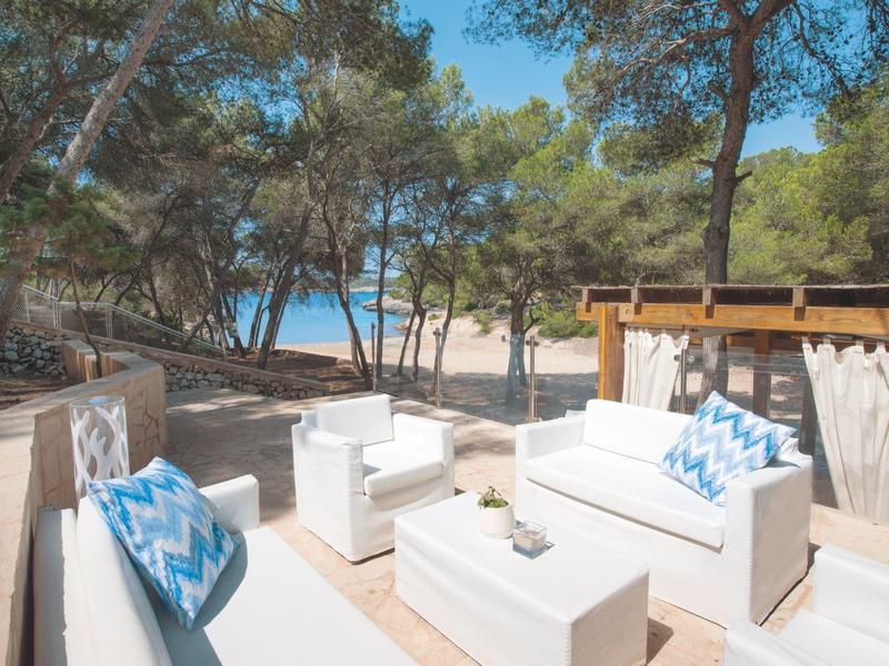 Taras z białymi meblami wypoczynkowymi, widok na śródziemnomorskie drzewa i morze