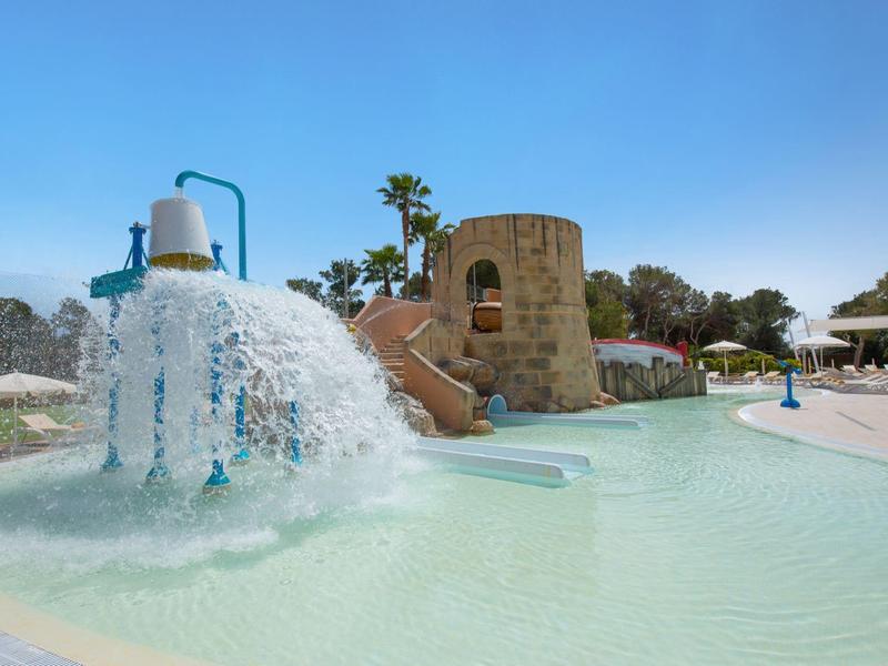 Kolorowy plac zabaw wodny z zjeżdżalnią i sztucznym wodospadem w basenie przy czystym niebie.