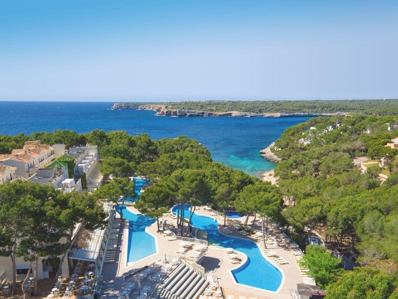 Widok na basen hotelowy z morzem i zalesionym wybrzeżem w tle.