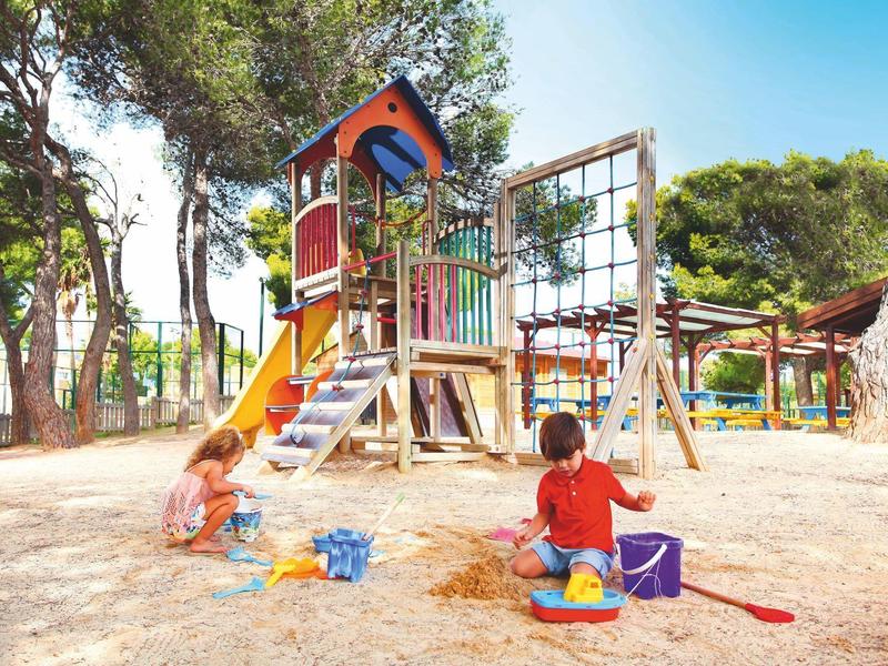 Dzieci bawiące się na placu zabaw z zjeżdżalnią i piaskownicą na świeżym powietrzu.