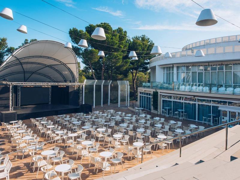 Miejsce na wydarzenia na świeżym powietrzu z sceną i licznymi stolikami oraz krzesłami pod czystym niebem.