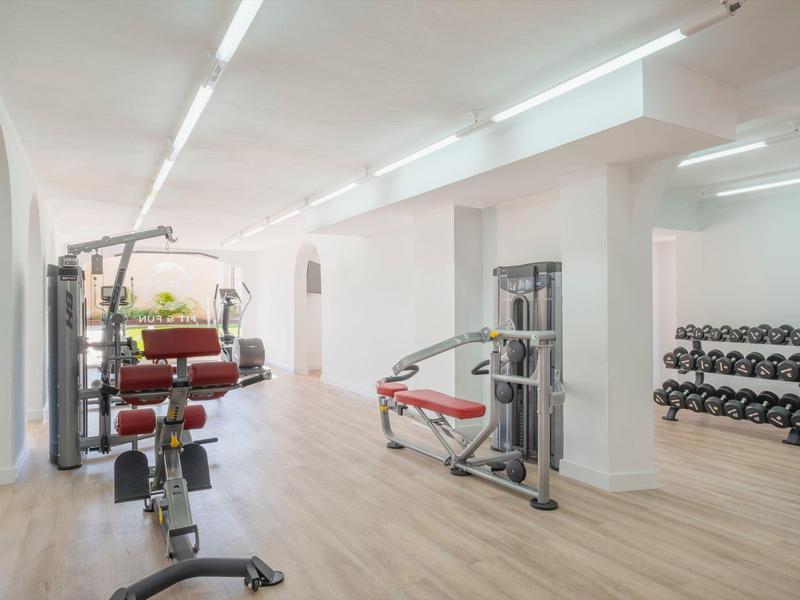 Jasna siłownia z urządzeniami, hantlami i drewnianą podłogą w nowoczesnym wnętrzu.