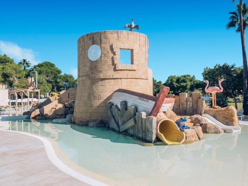 Plac zabaw wodny dla dzieci z wieżą, zjeżdżalnią i flamingami obok basenu