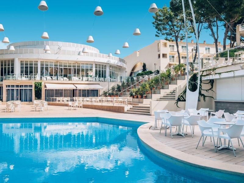 Nowoczesny basen hotelowy z białymi meblami i wiszącymi światłami na zewnątrz.