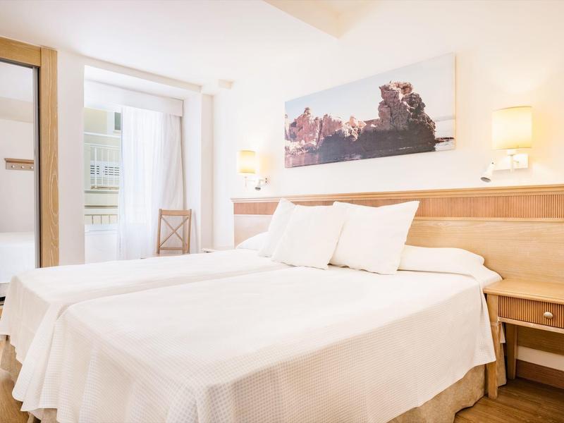 Jasny pokój hotelowy z dwoma łóżkami pojedynczymi, drewnianymi meblami i obrazem nad zagłówkiem.