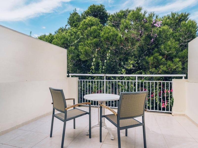 Balkon z stołem i trzema krzesłami na tle zielonych drzew pod niebieskim niebem.