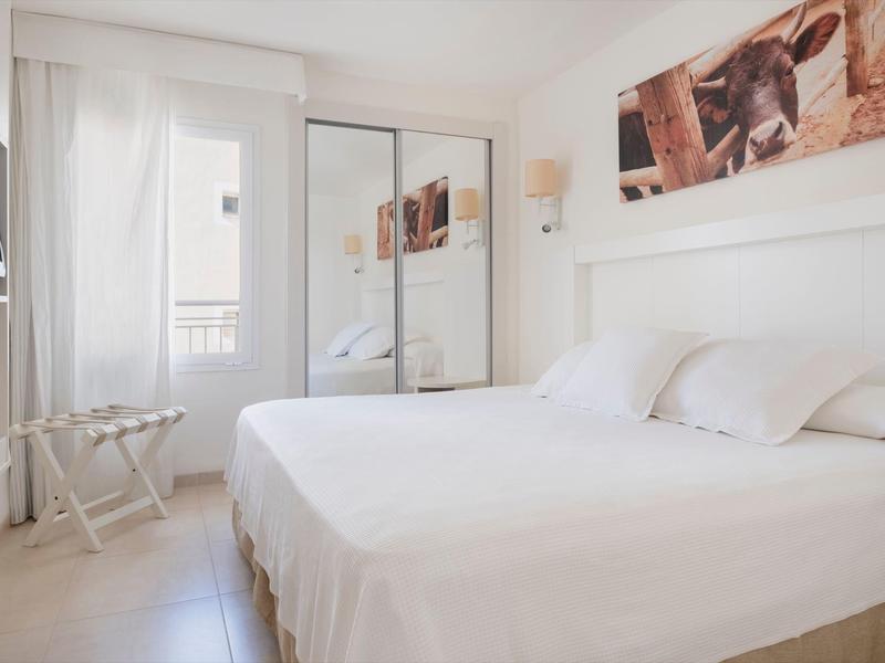 Jasny pokój hotelowy z podwójnym łóżkiem, dużym lustrem i drzwiami balkonowymi.