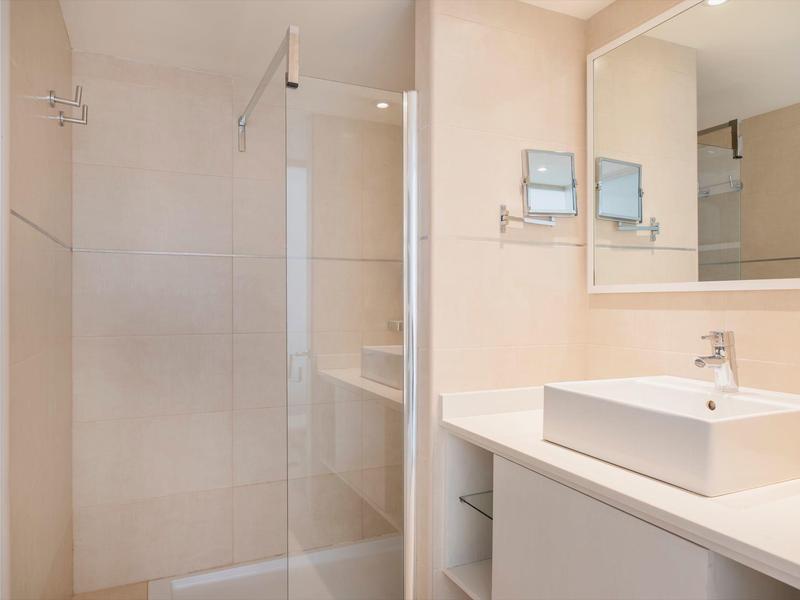 Nowoczesna łazienka z szklaną kabiną prysznicową, białą umywalką i dużym lustrem.