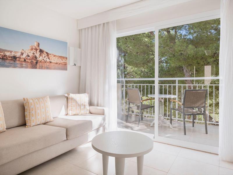 Jasny salon z sofą i balkonem z widokiem na zielone drzewa.