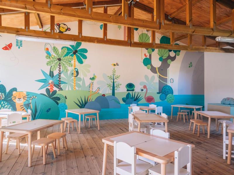 Jasne pomieszczenie z drewnianymi stołami i kolorowymi muralami w hotelu.