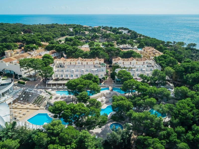 Zdjęcie z lotu ptaka hotelu z basenami otoczonego drzewami nad brzegiem morza.