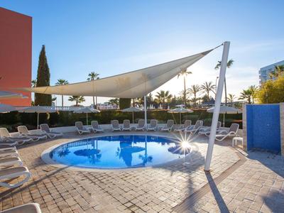 Small circular pool with sunshades and lounge chairs in a sunny outdoor hotel area.