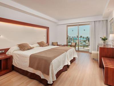 Bright hotel room with double bed, beige decor, wooden furniture, and balcony view.