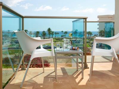 Balcony with white chairs, table, and sea view under a partly cloudy sky.