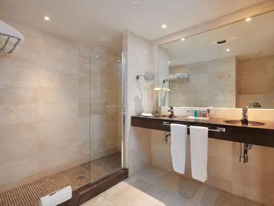 Modern bathroom with glass shower, large mirror, double sink, and beige tiled walls.