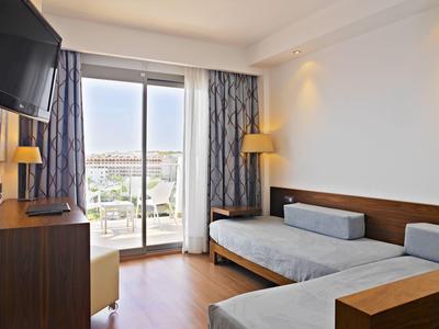 Bright hotel room with two single beds, TV, wooden furniture, and balcony with city view.