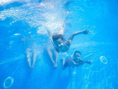 Two people swimming underwater in a clear blue pool with bubbles around them.