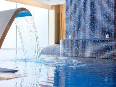Indoor pool with cascading water feature and blue mosaic tiles.