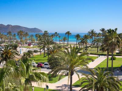 Resort with palm trees, parking, and ocean view under a clear sky.