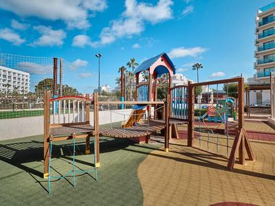 Sunny outdoor playground with climbing structures and slides between hotel buildings.
