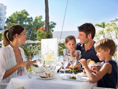 Family enjoying meal on terrace with pool in background.