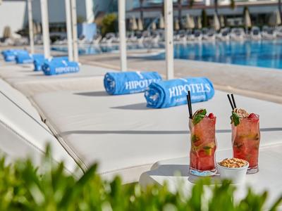 Two colorful cocktails and nuts on a table next to a lounge chair by the pool with blue towels.