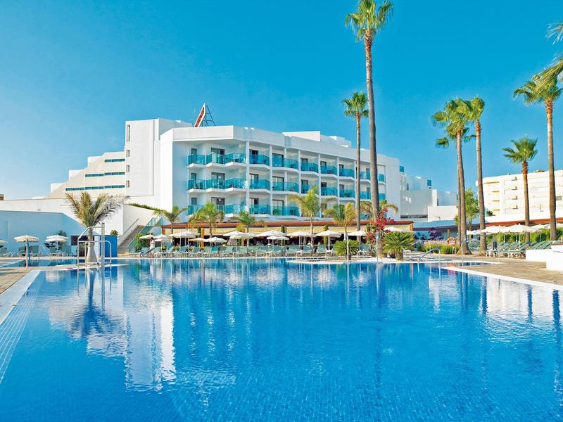 Modern hotel with pool, palm trees, and clear blue sky on a sunny day.