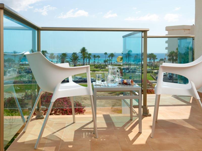 Balcony with white chairs, table, and sea view under a partly cloudy sky.