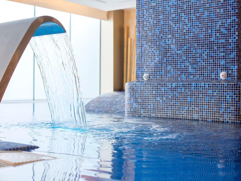 Indoor pool with cascading water feature and blue mosaic tiles.